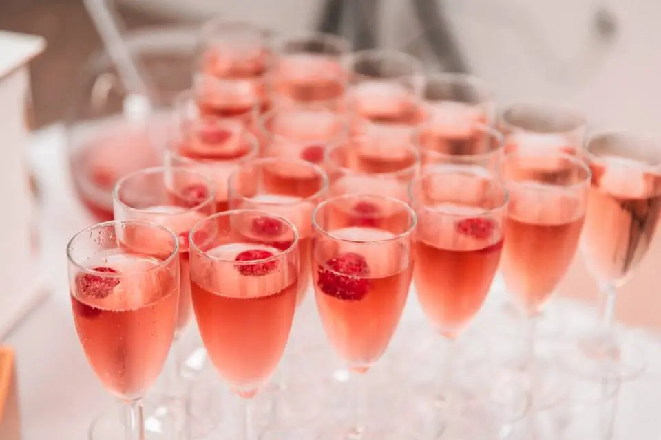 img-page-traiteur-emporter-verre Rangée de flûtes remplies d’un cocktail rouge à la framboise sur table de réception