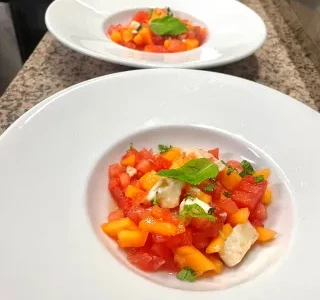 Duo de salades fraîches à base de tomates, pastèque, pêche et mozzarella, décorées de basilic Duo de salades fraîches à base de tomates, pastèque, pêche et mozzarella, décorées de basilic