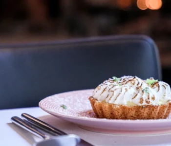 Tarte au citron meringuée posée sur une assiette rose, servie sur une table élégante avec couvert dressé, au coin du feu