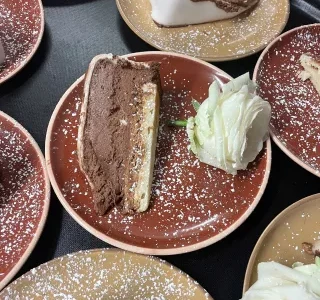 Part de gâteau au chocolat noir et biscuit croustillant, servie avec une rose blanche décorative sur une assiette rouge Part de gâteau au chocolat noir et biscuit croustillant, servie avec une rose blanche décorative sur une assiette rouge