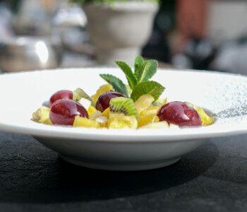 Assiette de salade de fruits colorée avec raisins rouges, kiwi, ananas et menthe fraîche, servie dans une assiette blanche en extérieur Assiette de salade de fruits colorée avec raisins rouges, kiwi, ananas et menthe fraîche, servie dans une assiette blanche en extérieur