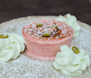 Entremets rose garni de pistaches et de chantilly verte, sur assiette céramique beige