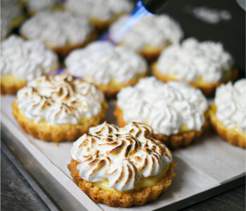 Tartes au citron meringuées alignées en cuisine pendant le brûlage de la meringue au chalumeau Tartes au citron meringuées alignées en cuisine pendant le brûlage de la meringue au chalumeau