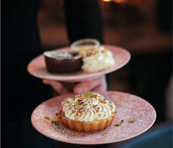 Serveur portant deux assiettes avec une tarte au citron meringuée et un moelleux au chocolat, ambiance chaleureuse au coin du feu Serveur portant deux assiettes avec une tarte au citron meringuée et un moelleux au chocolat, ambiance chaleureuse au coin du feu