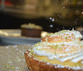 Tarte au citron meringuée garnie de zestes de citron vert et de sucre glace, prise en gros plan pendant le saupoudrage Tarte au citron meringuée garnie de zestes de citron vert et de sucre glace, prise en gros plan pendant le saupoudrage