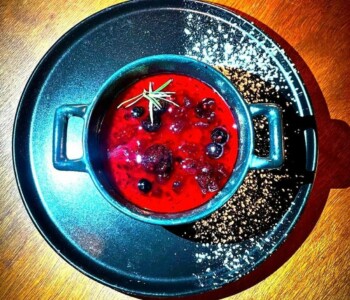 Panna cotta maison, fruits rouges & touche de romarin Panna cotta aux fruits rouges dans une cocotte sur assiette noire, décorée de sucre glace