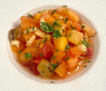 Salade de fruits frais de saison & touche de menthe Salade de fruits frais avec menthe, servie dans une assiette blanche